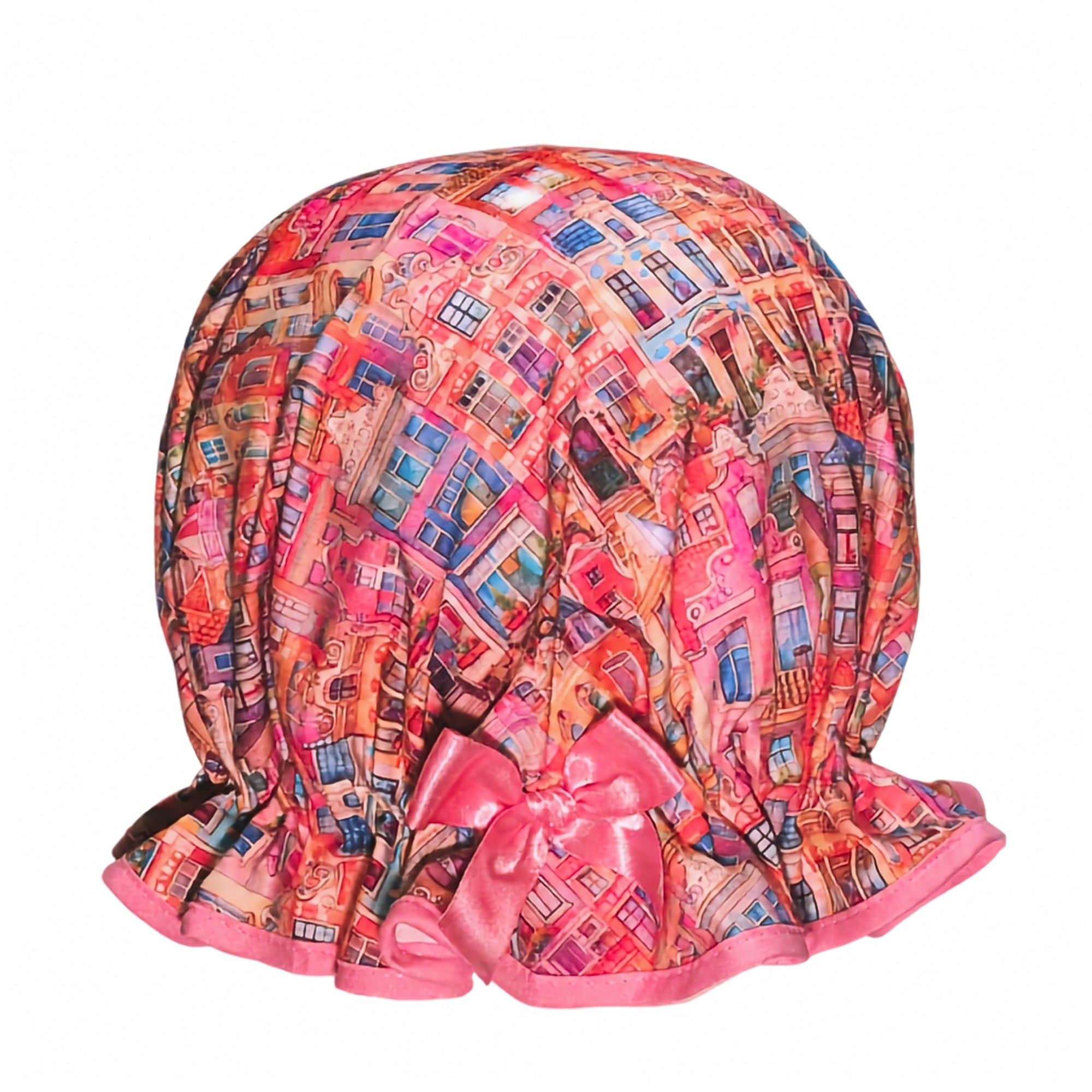 Vintage style women's roomy cotton shower cap. Frilled edge, colourful townhouse print in warm sun set feel tones of pink, orange and purple. Trimmed in a warm pink with matching satin bow.