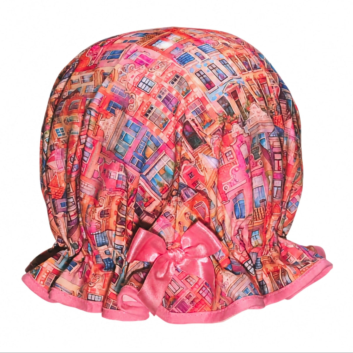 Vintage style women's roomy cotton shower cap. Frilled edge, colourful townhouse print in warm sun set feel tones of pink, orange and purple. Trimmed in a warm pink with matching satin bow.