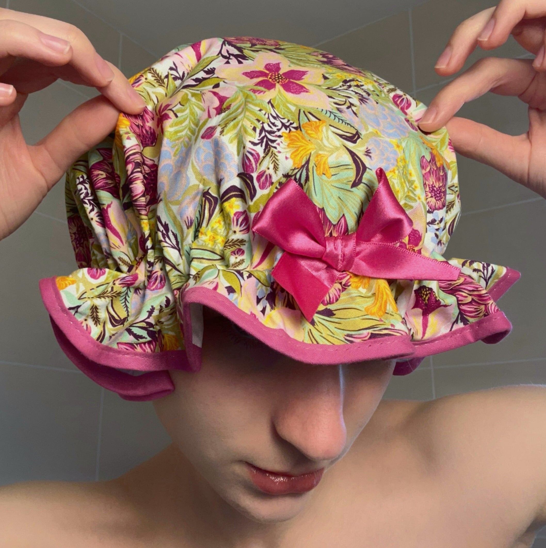 Woman wearing a colourful floral shower cap with a pink bow.