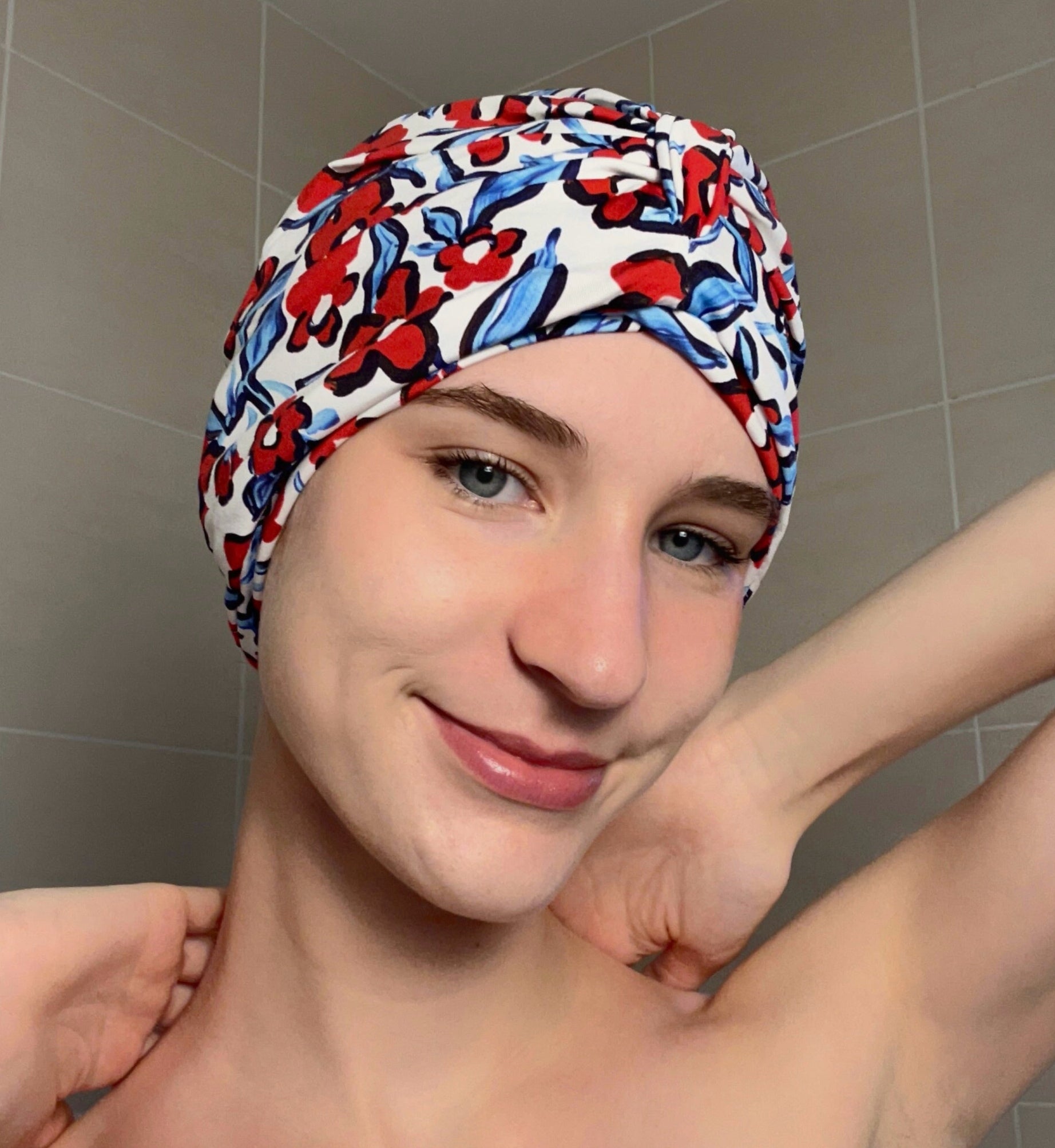 Woman wearing a colourful blue and red floral-patterned shower turban in a tiled bathroom.