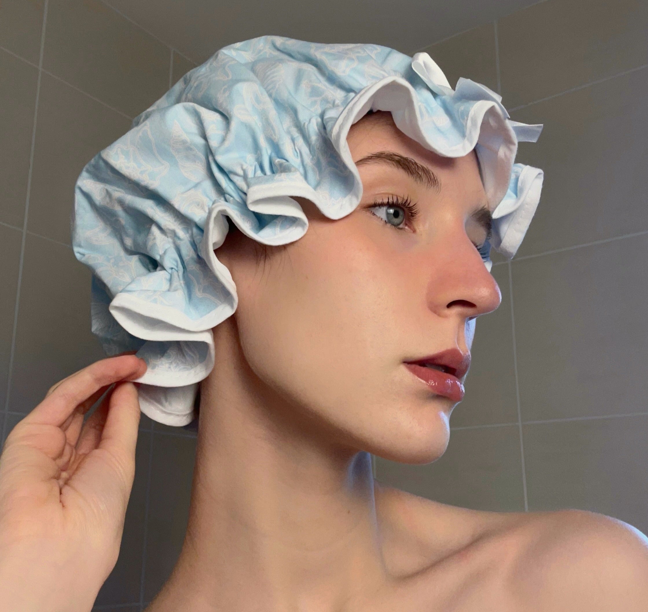 Woman wearing a blue and white sea shell print shower cap in a bathroom setting