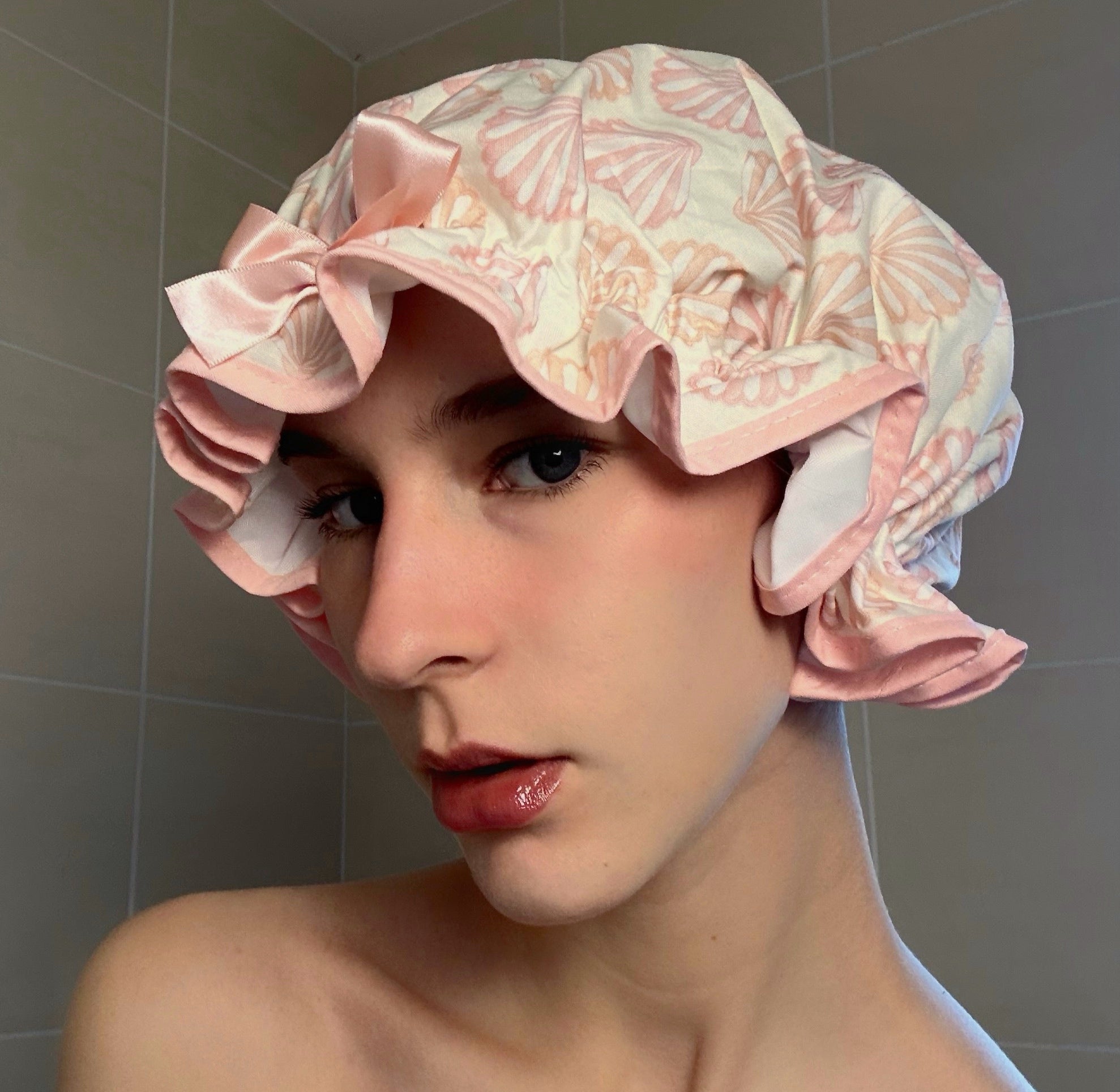 Woman wearing a coral shell shower cap in a bathroom setting