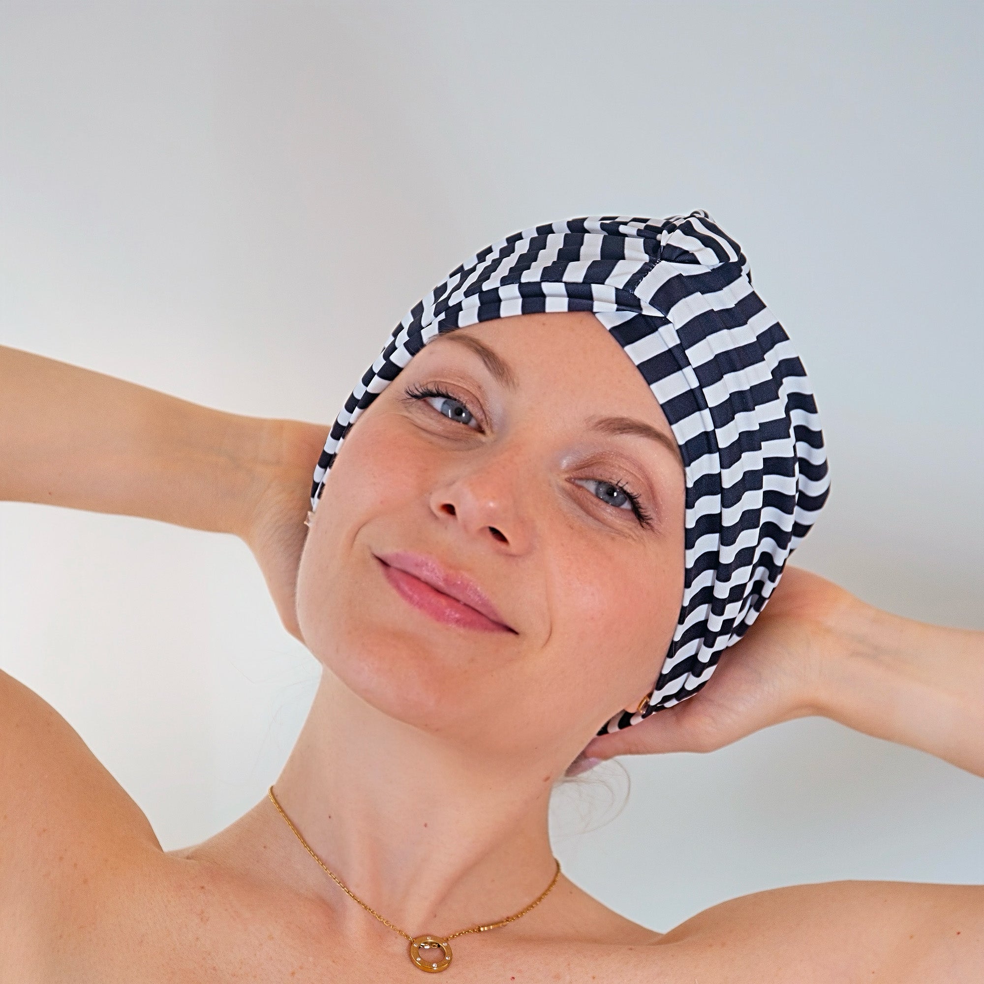 Woman wearing a black and white striped shower cap against a plain background