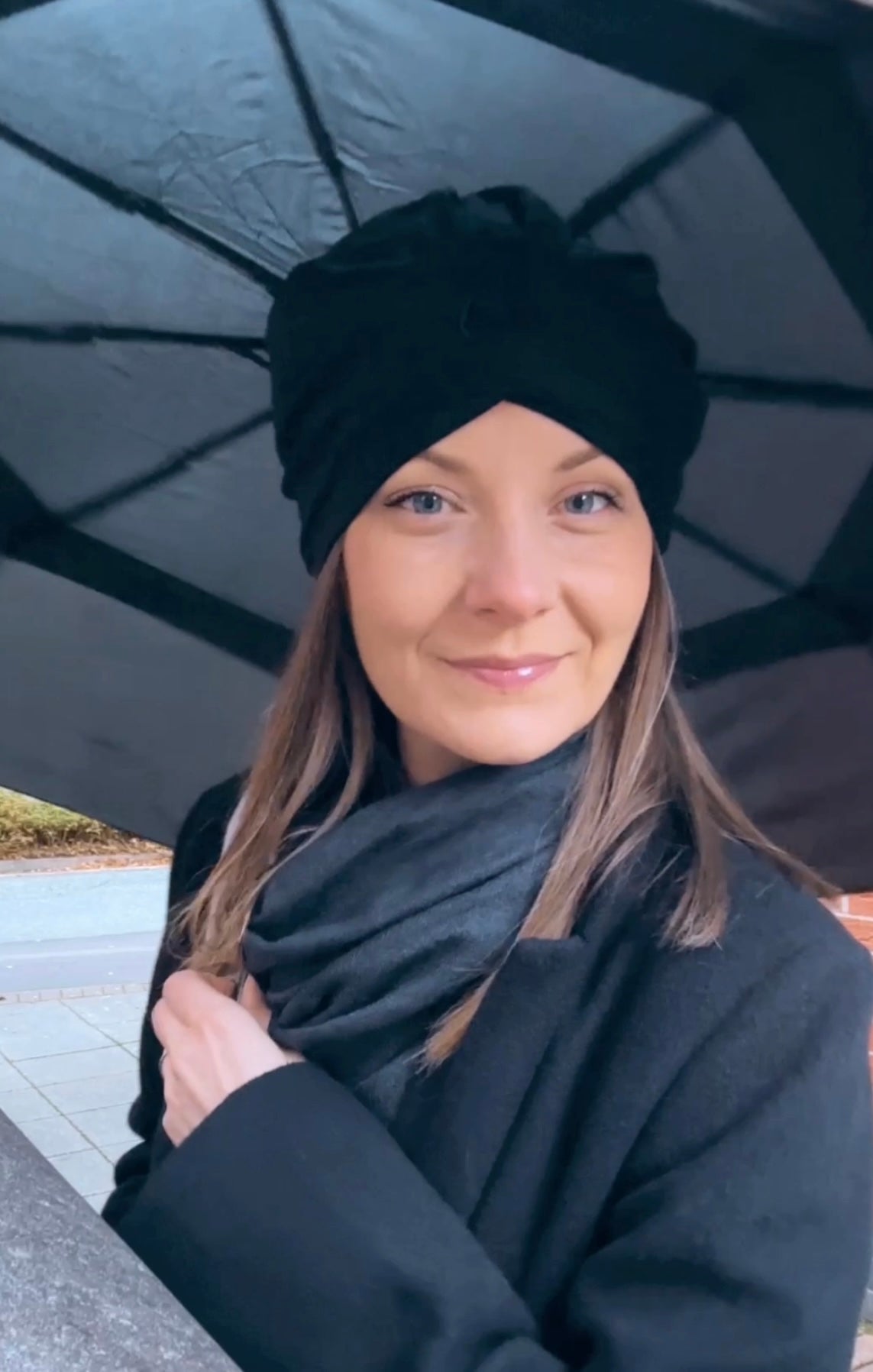Woman wearing a black turban and coat holding an umbrella