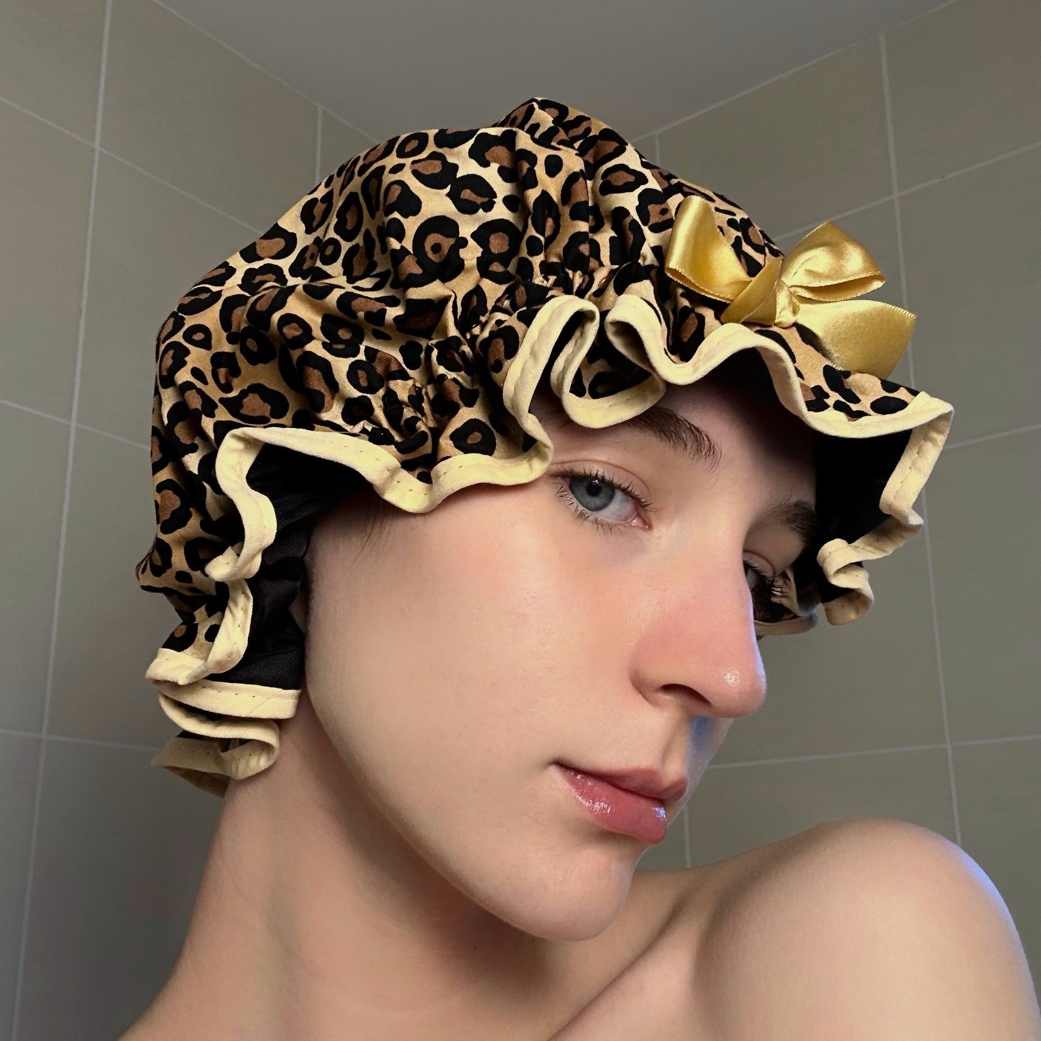 Woman wearing a leopard print shower cap with a beige bow in a bathroom setting